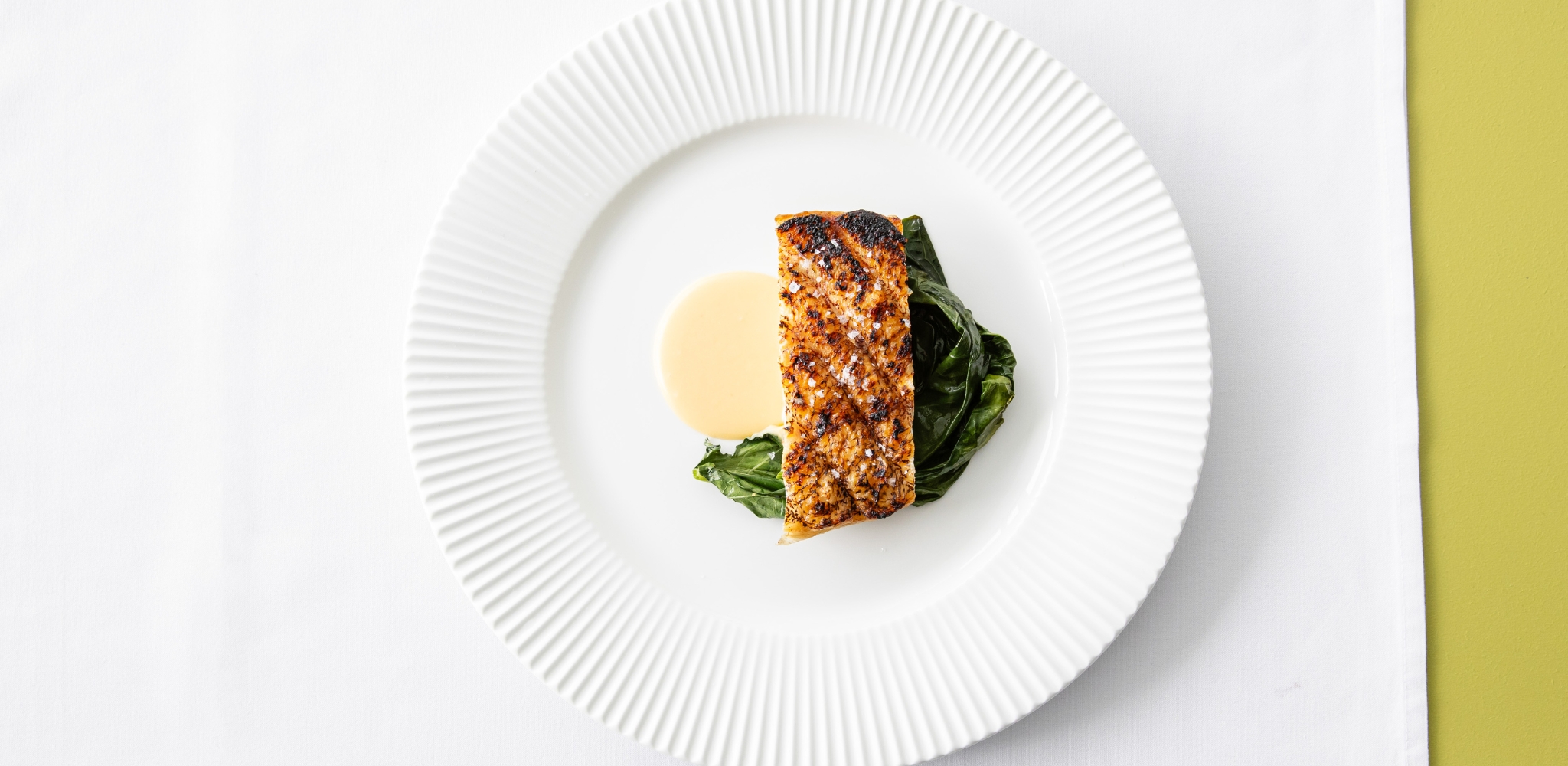 Image of Chris Bolton Coral Trout with Limoncello Beurre Blanc and greens on a large white plate with white linen served at Bistro George.