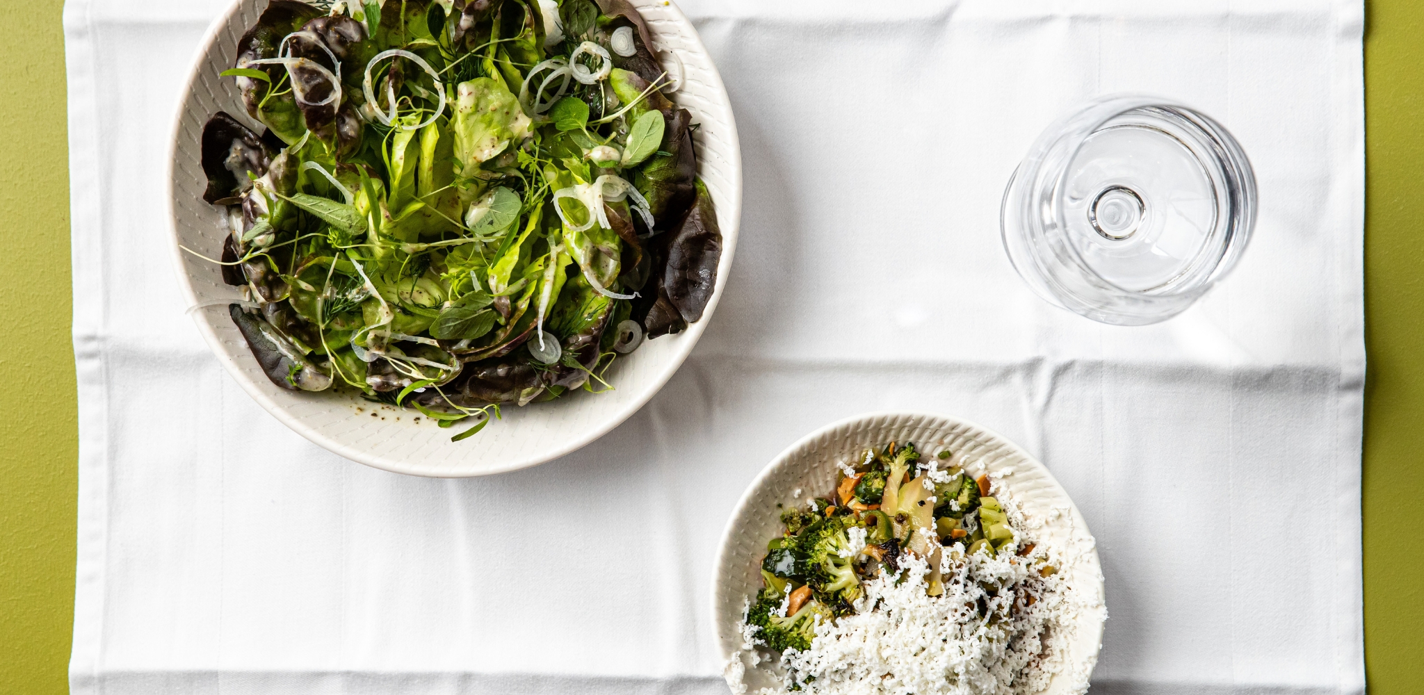 Image of a white bowl with Ramarro Farm Leaves, a white bowl with Charcoal Grilled Broccoli Salad and a wine glass served at Bistro George in the Sydney CBD venue, Jacksons on George.