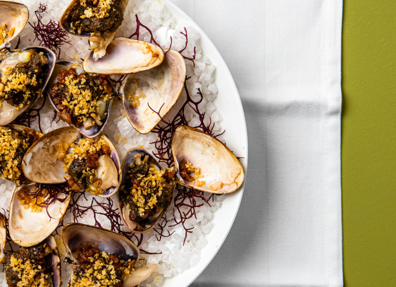 Image of Clams Casino with Café de Paris butter, crispy Guanciale and pangratatto served on a white plate at Jacksons on George.