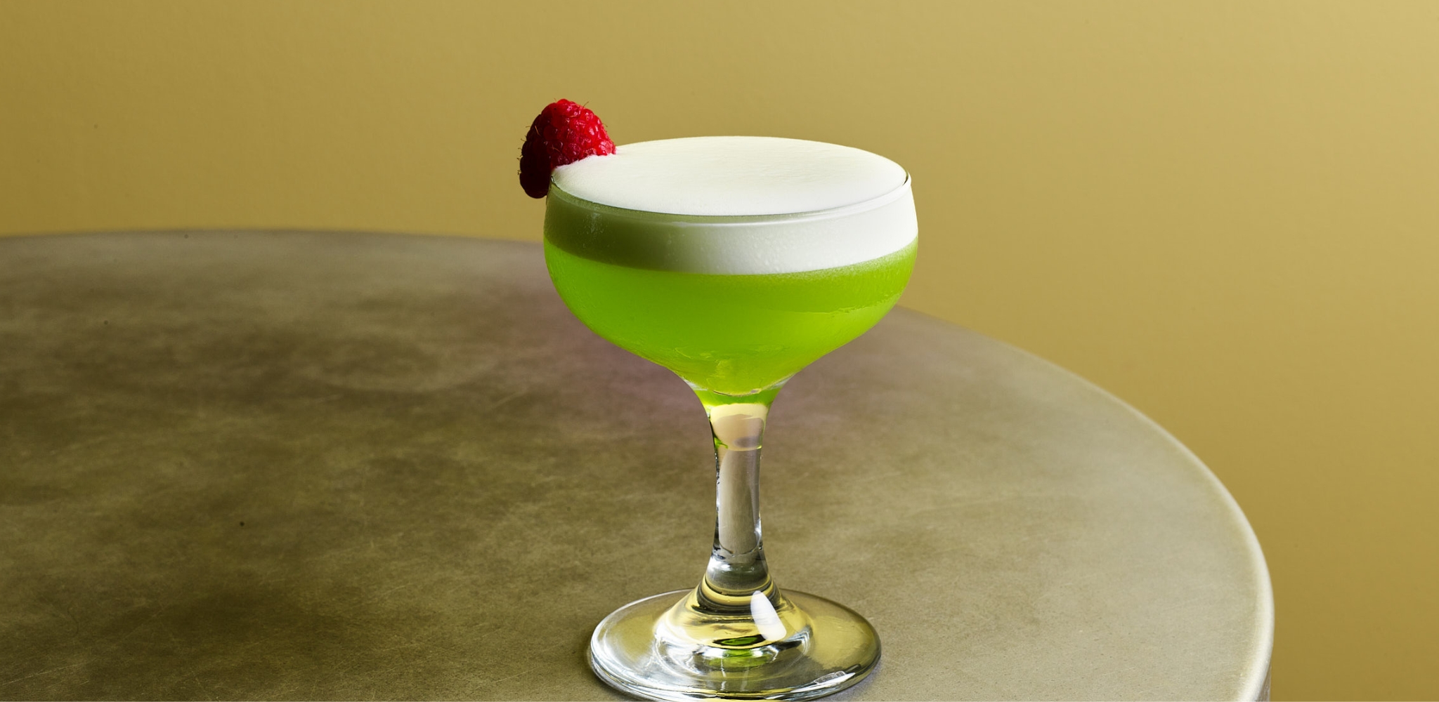 Image of the Jacksons Slipper cocktail with Ketel One Citroen, Midori, yuzu, lemon, whites with a raspberry on a stainless steel table.