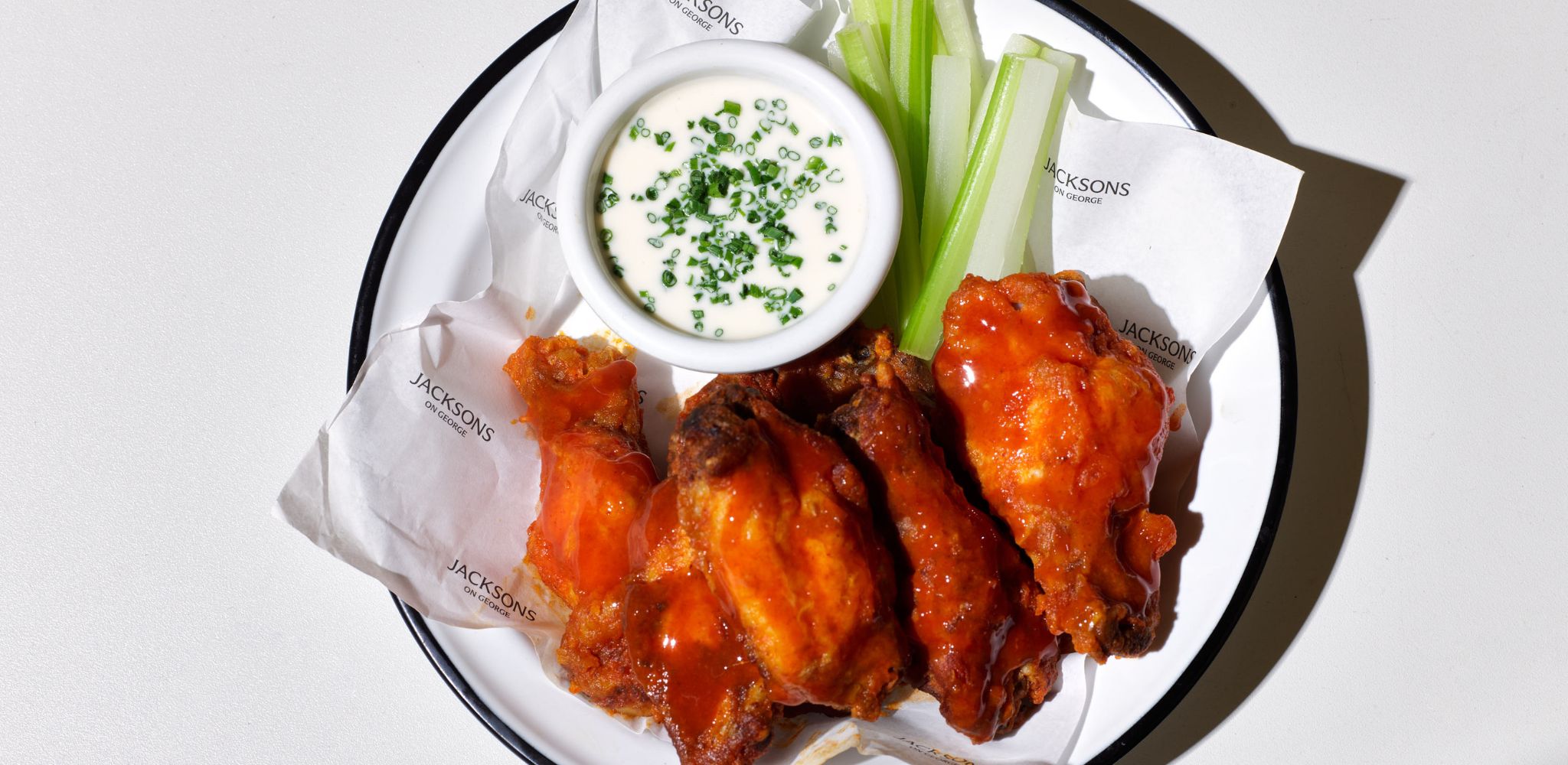 Buffalo fried chicken wings, with blue cheese sauce, chives and celery served on Jacksons on George logo