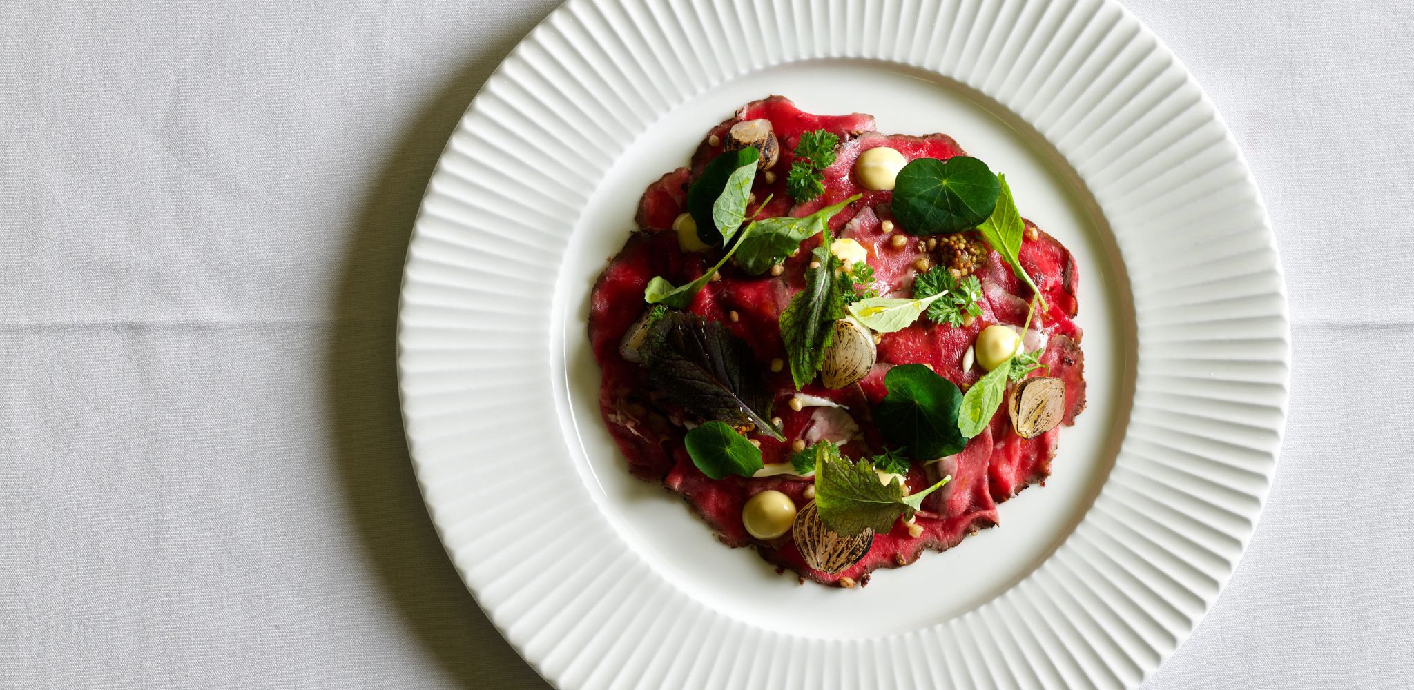 Image of Westholme dry aged Wagyu beef carpaccio on a white plate with a white table cloth.